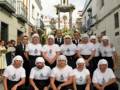 Un grupo de personas vestidas con camisetas blancas y gorros blancos posan en una calle con un altar de flores al fondo.