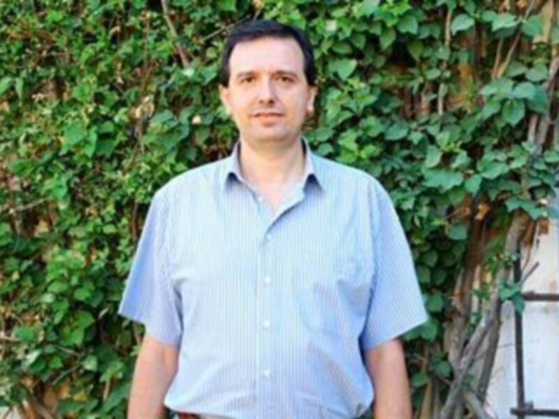 Hombre sonriente frente a una pared de hojas verdes