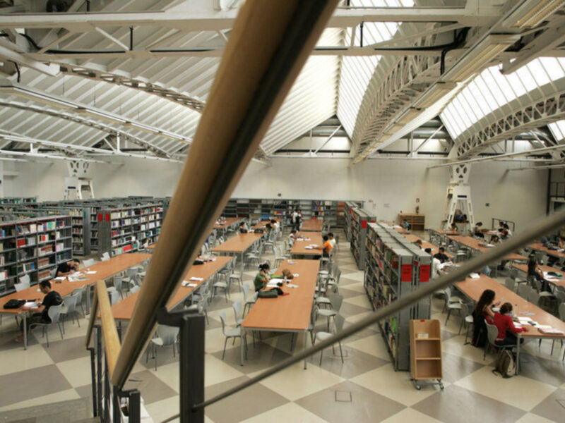 Interior de una biblioteca moderna con estanterías y mesas de estudio, donde estudiantes están trabajando.
