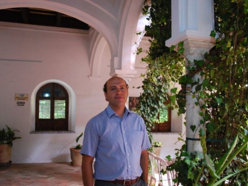 Un hombre en una casa colonial con plantas y una puerta de madera en el fondo.
