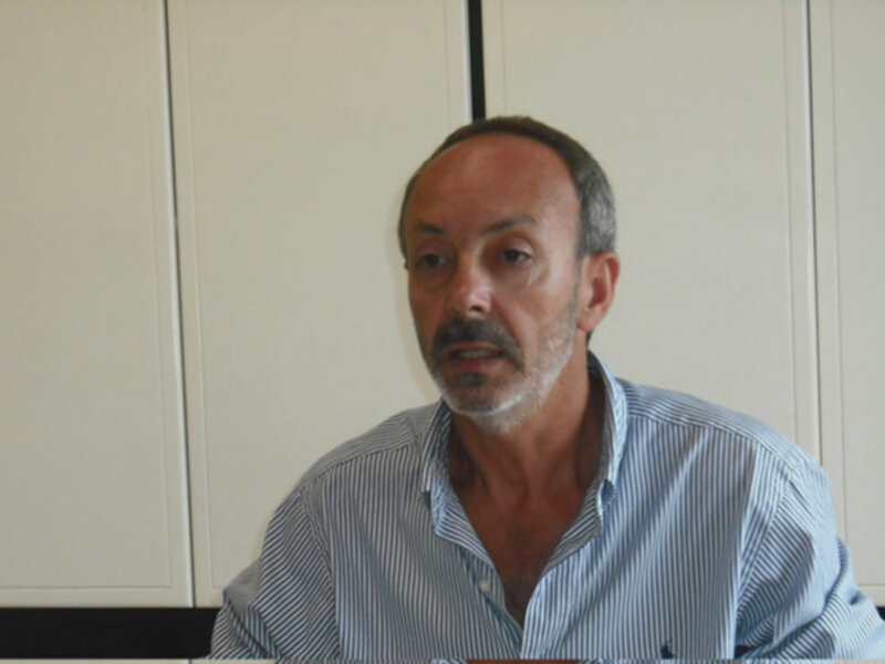 Hombre con camisa a rayas hablando en un entorno interior.