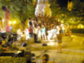 Concierto al aire libre en una plaza nocturna, con público disfrutando de la música en un escenario iluminado.