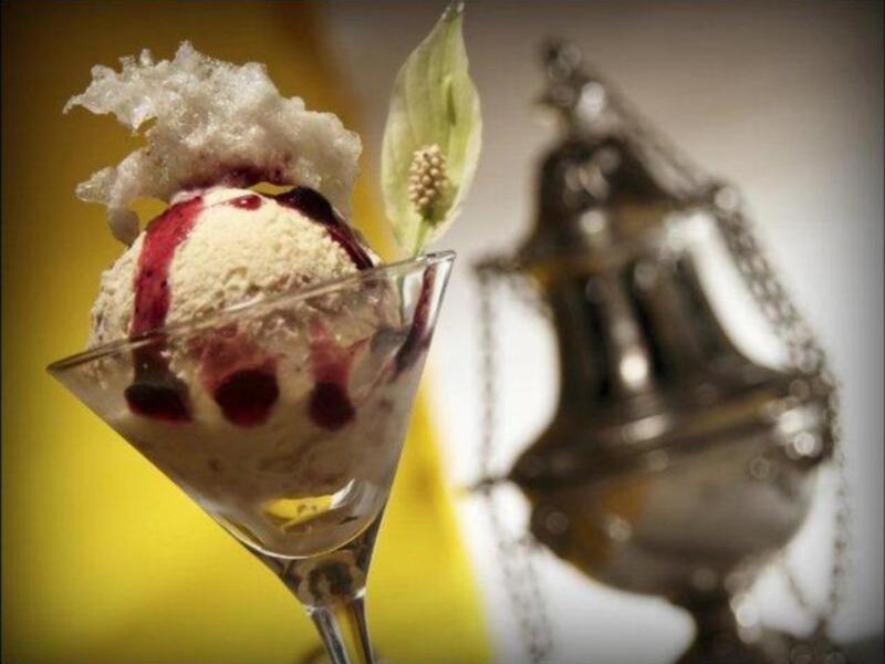 Helado artesanal con frambuesa y granos de café en copa de cristal, decorado con hoja de menta.