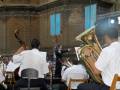 Orquesta en una iglesia, músicos tocan instrumentos como violín y tuba, director al frente.