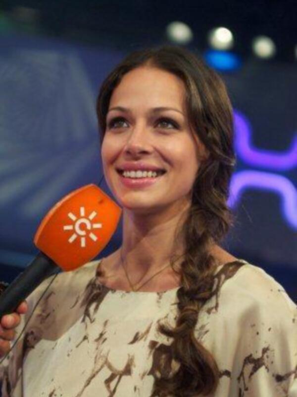 Entrevista en vivo con una presentadora sonriente sosteniendo un micrófono con logo de canal.