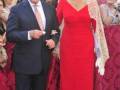 Una pareja elegante en un evento formal, el hombre con traje y la mujer con vestido rojo y velo dorado.