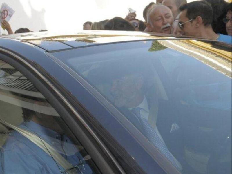 Persona en coche rodeada por una multitud de personas.