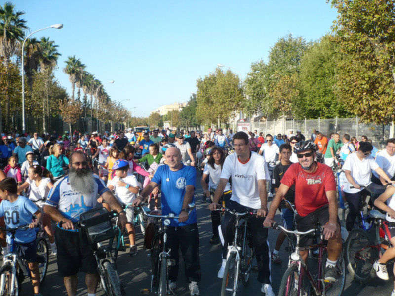 Marcha ciclista con participantes de todas las edades en una calle arbolada.