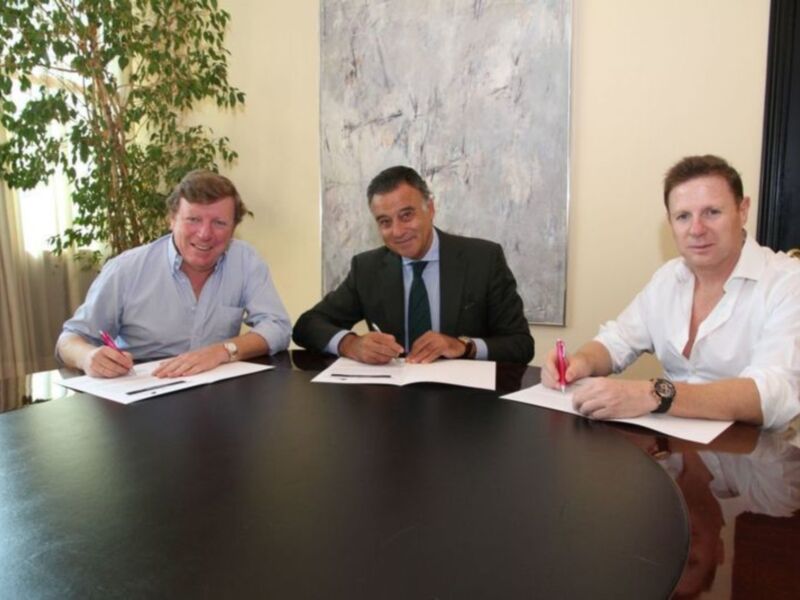 Tres personas firmando documentos en una reunión formal en un entorno profesional bien iluminado.