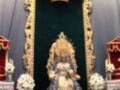 Imagen de la Virgen de la Esperanza, vestida con traje azul y corona dorada, en un altar ornamental con flores blancas.