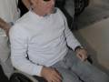 Un hombre en una silla de ruedas, con gafas de sol y una camiseta blanca. Detrás de él se ve a otra persona con un pañuelo blanco en la mano.