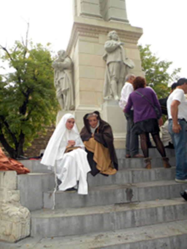 Personas vestidas con trajes históricos sentadas en las escaleras de un monumento con estatuas al fondo.