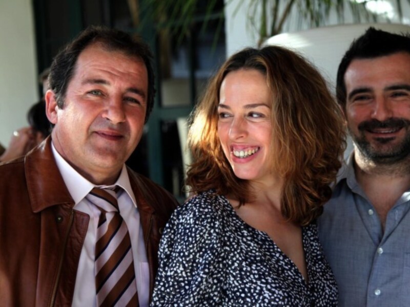 Tres personas sonrientes en una reunión, rodeadas de plantas y luz natural.