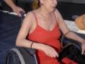 Una mujer en silla de ruedas con un vestido rojo, posiblemente en una celebración o evento público.