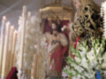 Imagen de una procesión religiosa con una imagen venerada en un altar dorado, rodeada por flores y velas.