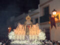 Procesión nocturna con la imagen de la Virgen María adornada con velas y flores, bajo la luz de una farola y el cielo oscuro.