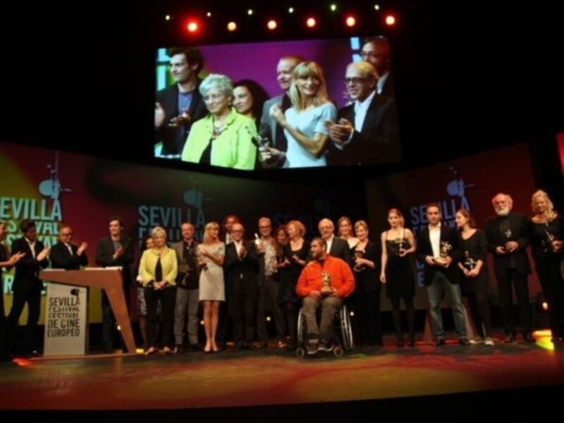 Ganadores de los premios del Festival de Cine de Sevilla 2016 en el escenario principal del festival, con una pantalla grande en el fondo que muestra el logo del festival y la fecha.