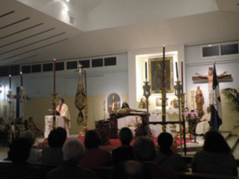 Interior de una iglesia durante una misa, con el sacerdote oficiando el servicio y el público asistiendo.