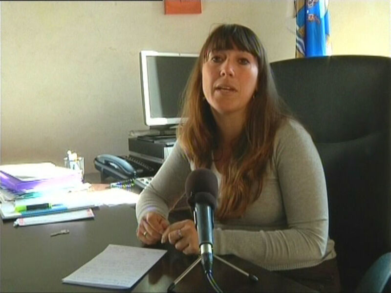 Entrevista en un estudio de radio o televisión, con una mujer sentada en una silla de oficina frente a un micrófono y un monitor de computadora en el fondo.