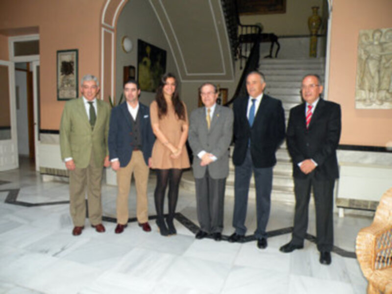 Grupo de personas en trajes y vestidos formales posando en un hall de estilo clásico.