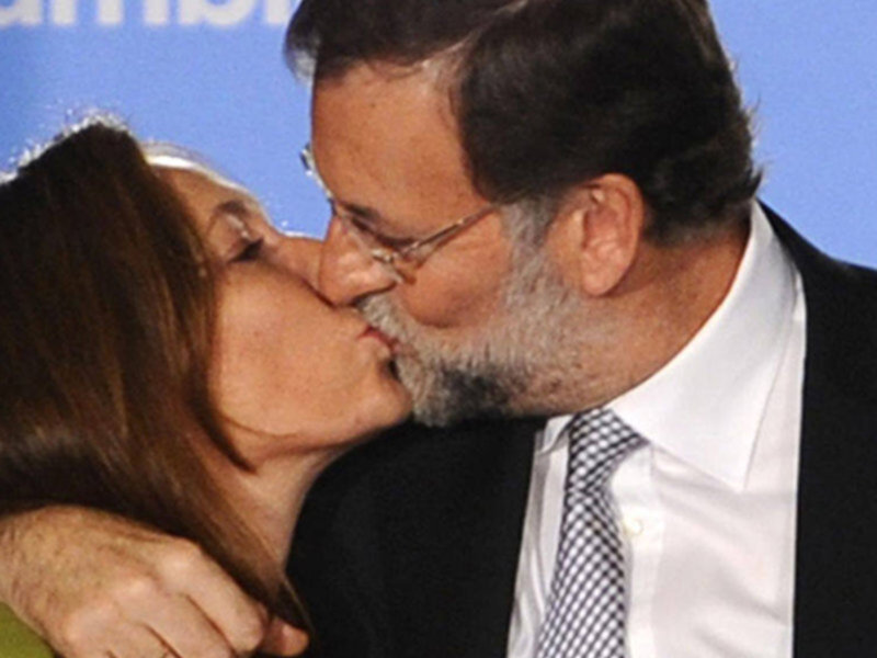 A close-up of a couple sharing a kiss, with a blue background that suggests a formal or celebratory event.