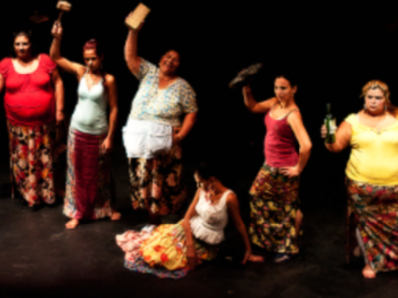 Una escena teatral con seis actores vestidos con trajes de colores vibrantes, posiblemente en un contexto de protesta o celebración.