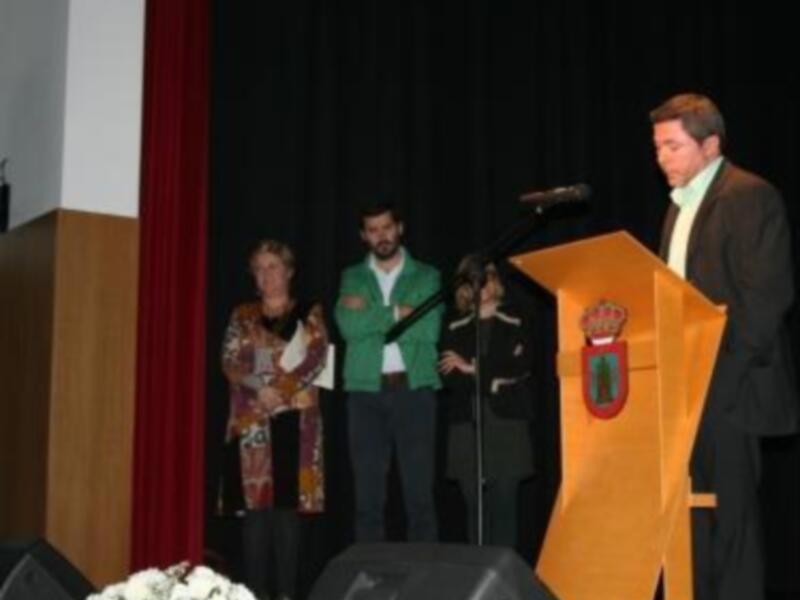Persona hablando en un podio durante una ceremonia con un escudo en el fondo.