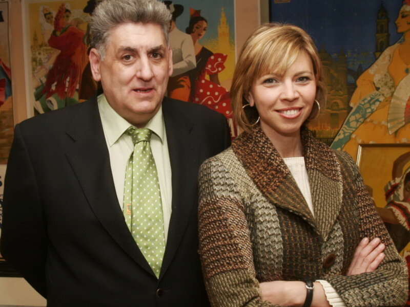Dos personas posan juntas frente a un fondo artístico con figuras humanas.