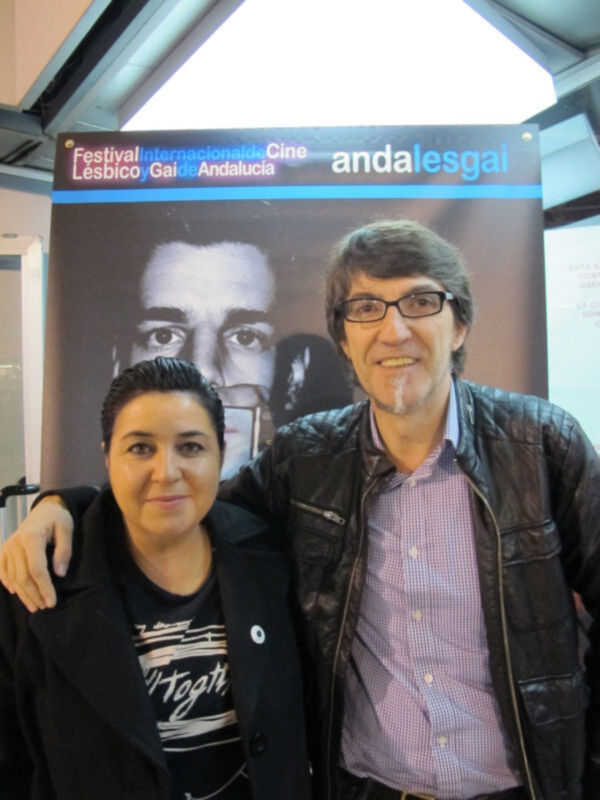 Dos personas posan frente a un cartel del Festival Internacional de Cine Lesbico y Gay de Andalucía.