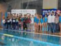 Equipo de natación posando en la piscina junto a patrocinadores.