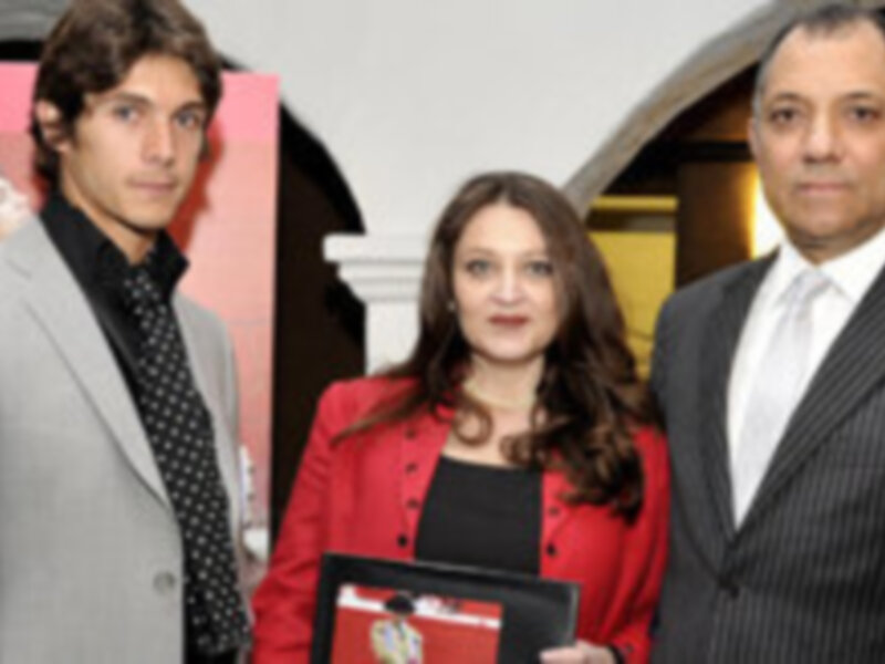 Un hombre vestido con traje negro y corbata, una mujer con blusa roja y pantalones negros, y un hombre con traje gris y corbata negra.