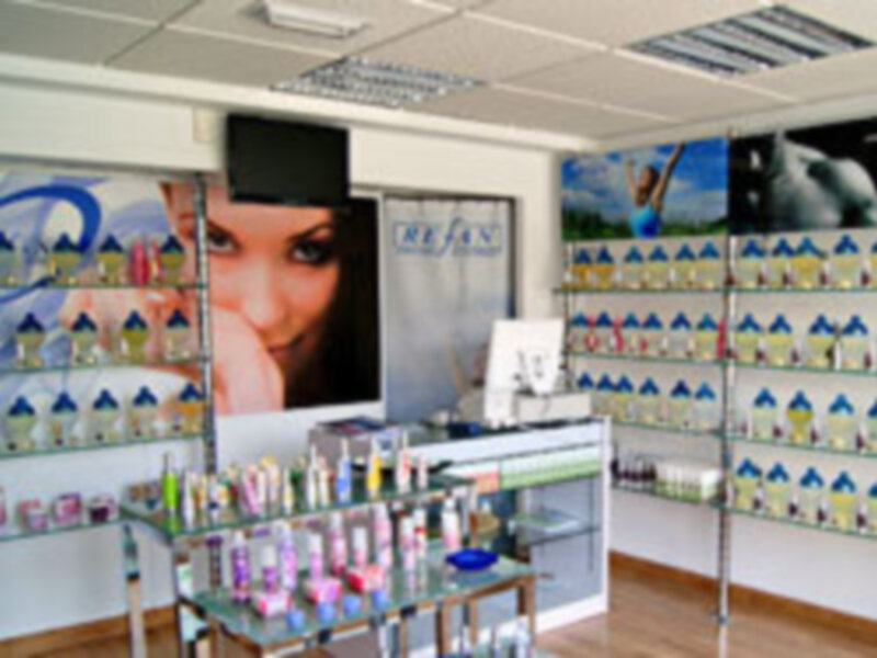 Salón de belleza con estanterías llenas de productos cosméticos y una pantalla de televisión en el fondo. La imagen muestra un ambiente de cuidado personal y estética.