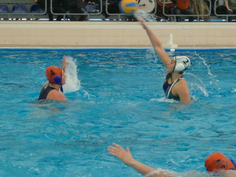 Jugadoras de waterpolo en acción durante un partido en una piscina cubierta.