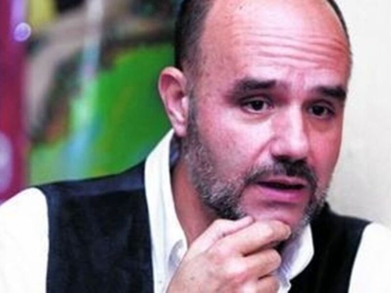 Un hombre con barba y camisa blanca, pensativo con la mano en la barbilla.