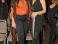 Dos mujeres posan juntas en un evento, una con un vestido naranja y otra con un vestido negro. La imagen muestra detalles de moda y estilo.