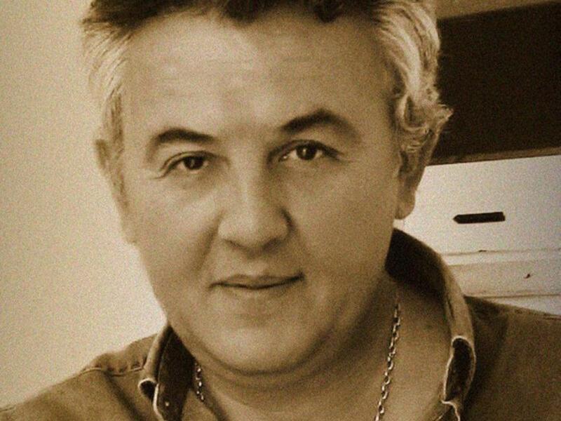 Retrato en blanco y negro de un hombre con cabello rizado y camisa abierta, expresión seria.