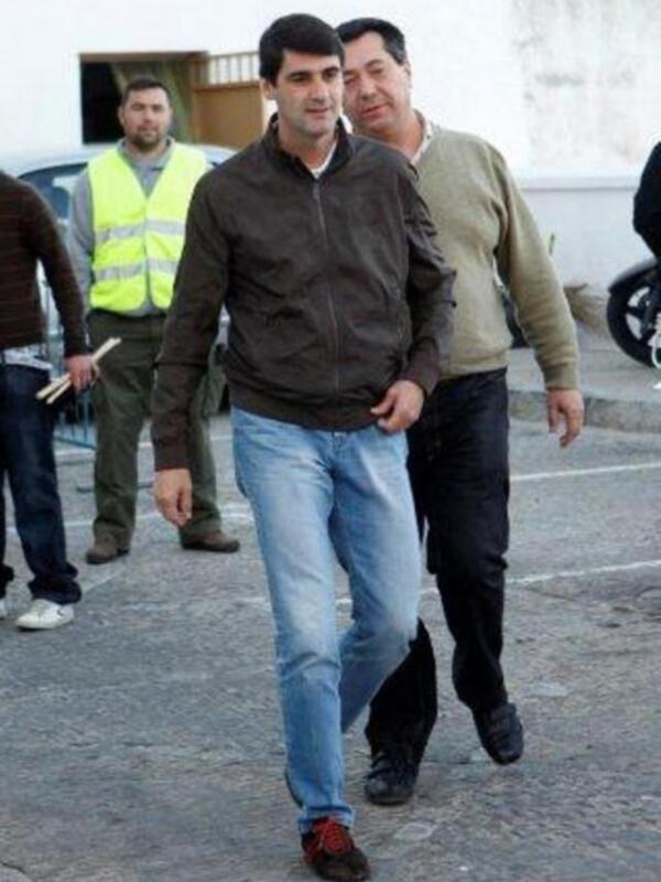 Dos hombres caminando por una calle, uno de ellos con una chaqueta marrón y otro con una camisa de lana beige.