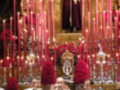 Una imagen de una iglesia con velas rojas encendidas en el altar, donde se puede ver a personas en trajes formales.