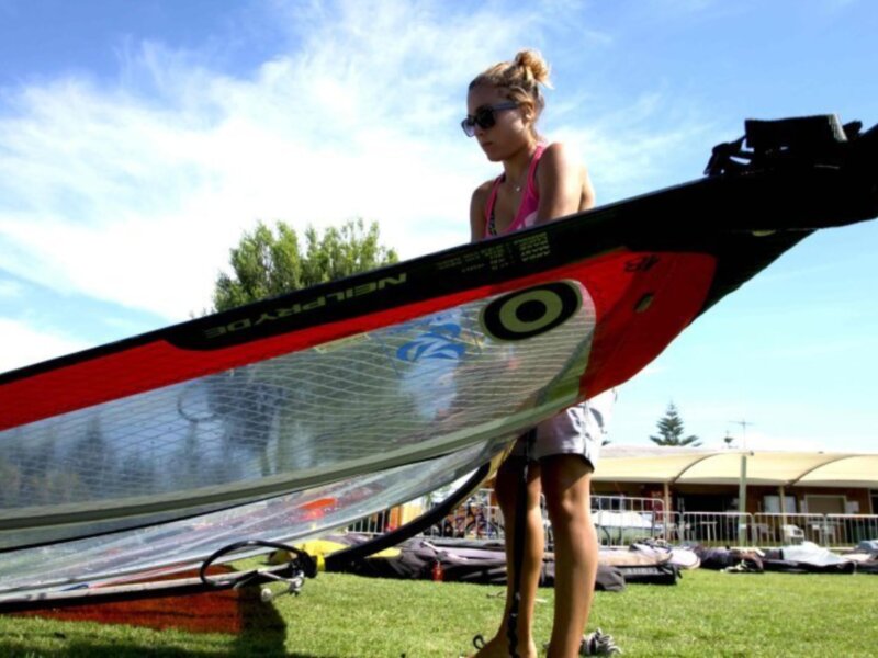 Una mujer sostiene un kayak de remo en un día soleado con un cielo azul claro y una casa en el fondo.
