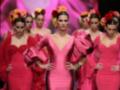 Modelos en trajes de flamenca rosa y rojo con flores en la cabeza, desfilando en un desfile de moda.