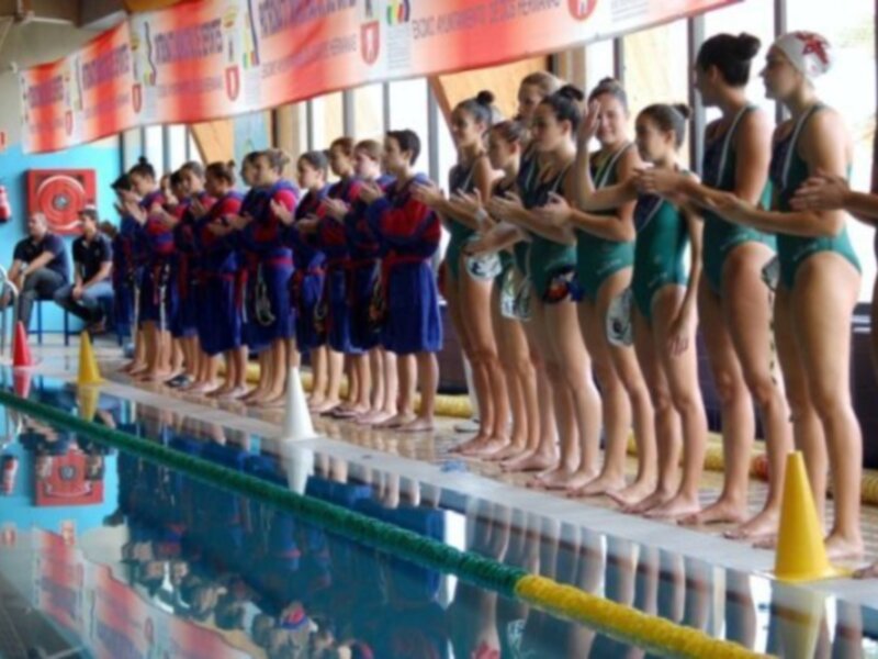 Equipo de natación femenino en la línea de arranque de una piscina, listo para competir.