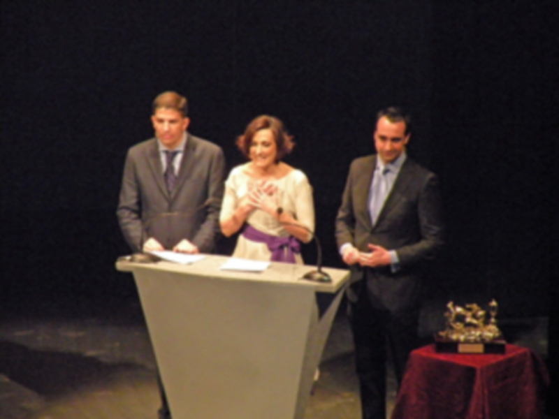Premio de honor en un evento formal en un escenario con un panel de tres personas.