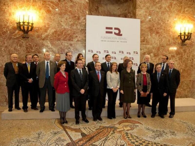 Grupo de personas posando en una sala con mosaicos en el suelo y una pancarta en el fondo.