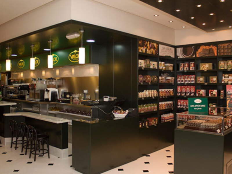 Interior de una tienda de café y productos de chocolate con mostrador de barra y estantes de productos.