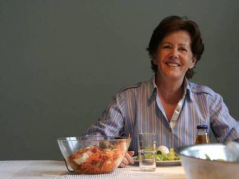 Una mujer sonríe mientras disfruta de una comida saludable en una mesa con platos de ensaladas y otros alimentos.