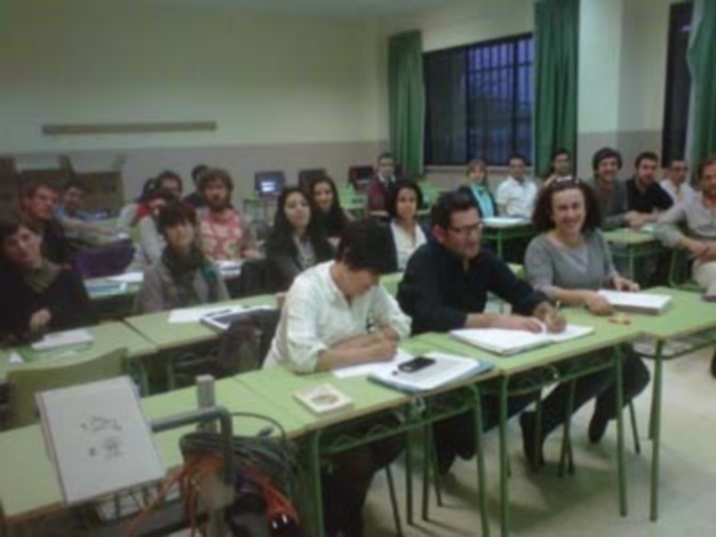 Un aula con estudiantes sentados en mesas, algunas tomando notas en cuadernos.