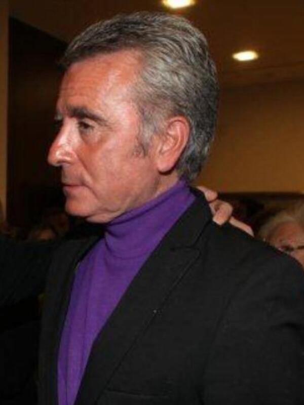 Un hombre con cabello gris y una camisa de color púrpura en un evento formal.