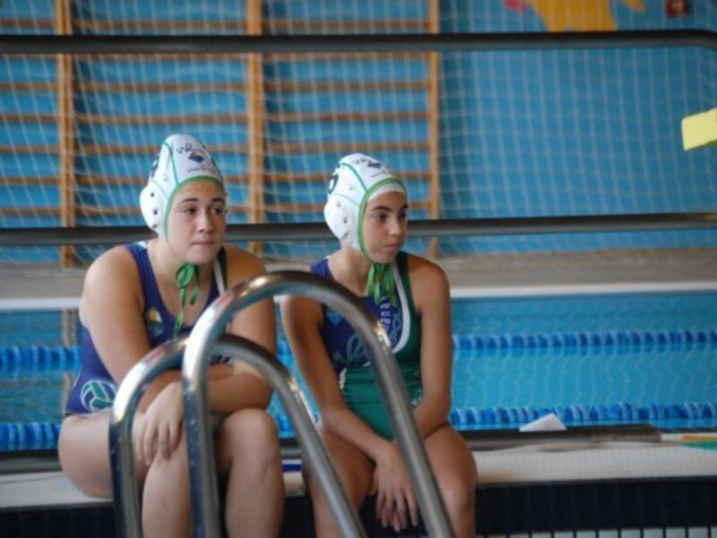 Jugadoras de waterpolo sentadas en el borde de una piscina, listas para un partido o entrenamiento.