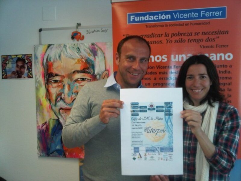 Un hombre y una mujer sostienen un cartel en una conferencia de la Fundación Vicente Ferrer, enfatizando la importancia de erradicar la pobreza y promover la humanidad.