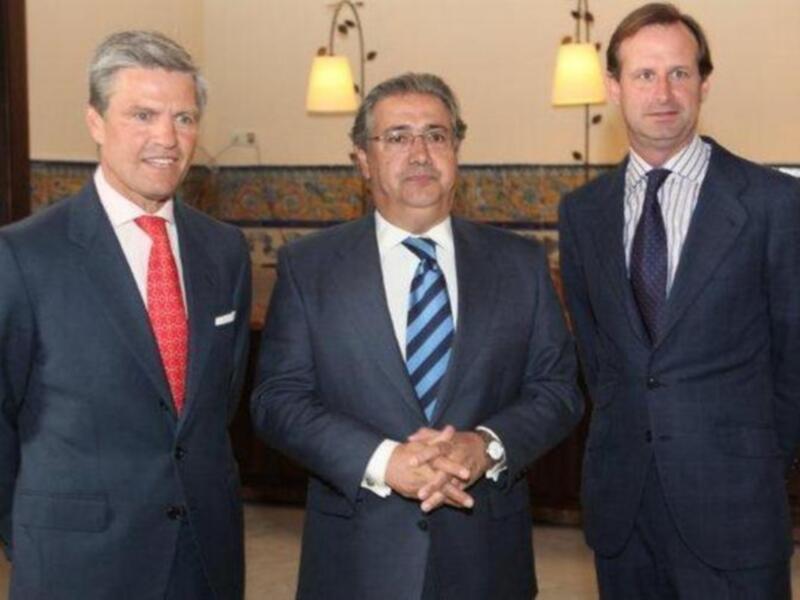 Tres hombres en trajes posando juntos en un interior formal.